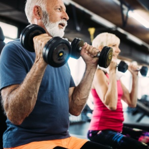 Two people in their 60s using weights in a gym.
